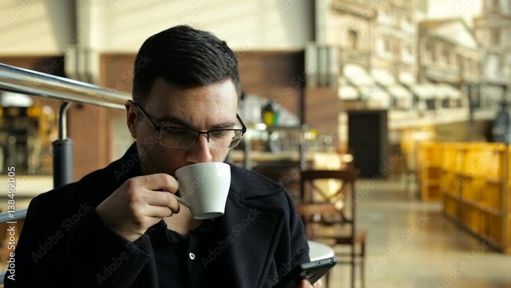 Adult male drinking coffee with a phone in his hand in cafes Adult male drinking coffee with a phone in his hand in cafes