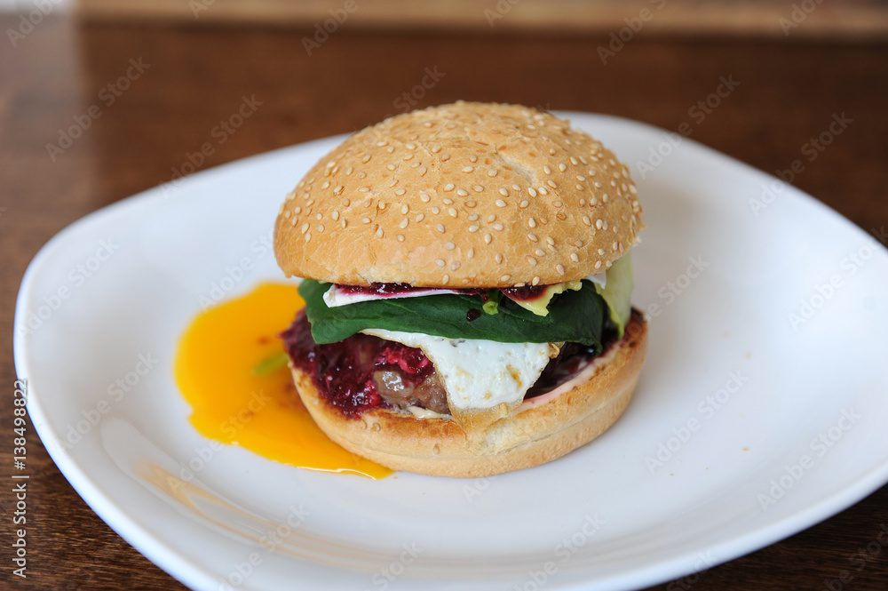 Burger with cutlet, vegetables, cheese and berry sauce closeup on a white plate on a wooden background