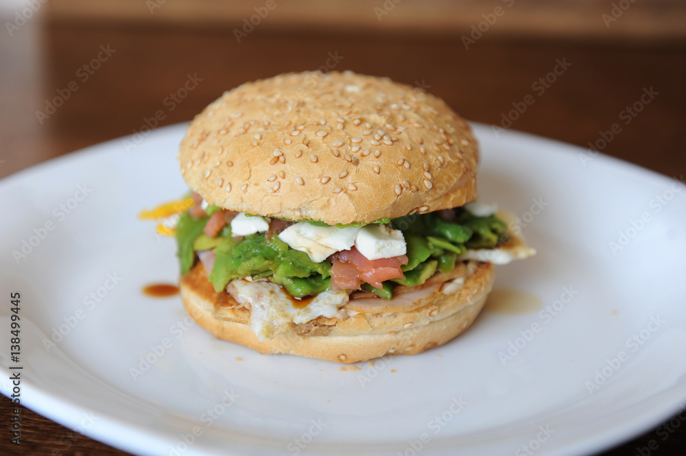 Burger with red fish, bacon, vegetables, cheese and berry sauce closeup on a white plate on a wooden background