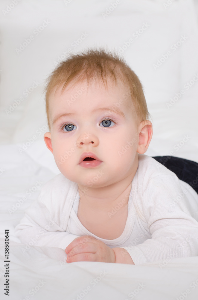 Adorable baby boy in white sunny bedroom relaxing in bed