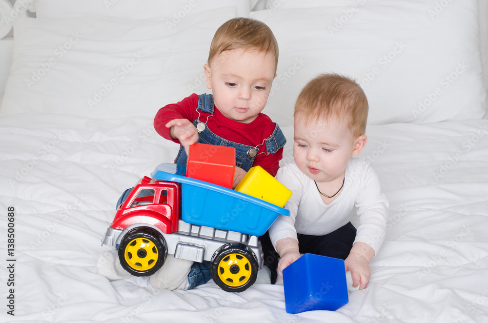 Two little children playing with color toys on white bed Two little children playing with color toys on white bed