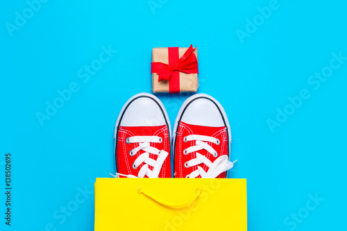 big red gumshoes in cool shopping bag and beautiful gift on the wonderful blue background photo