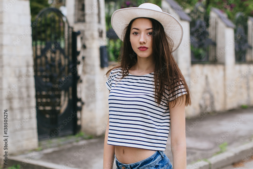 Beautiful girl in stylish jeans and white hat walking in the streets.
