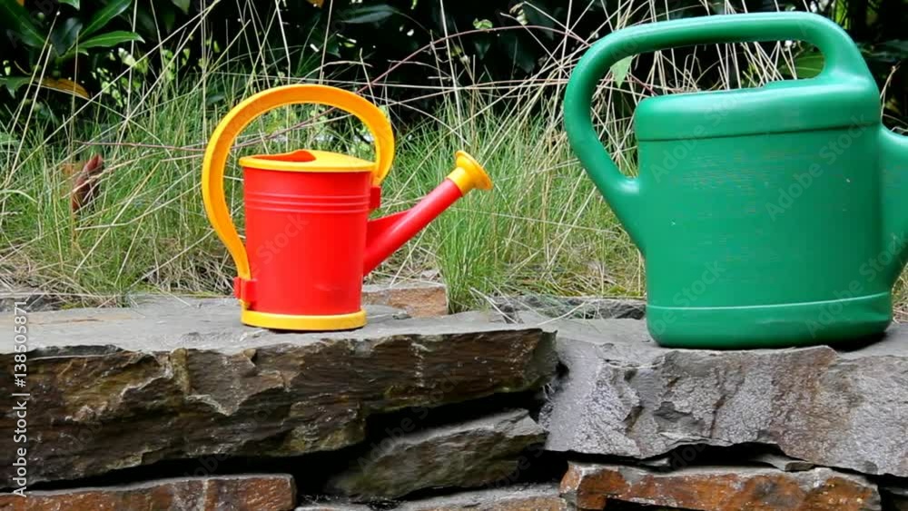 Green and Red Watering Cans on a Stone Retaining Wall in the Yard of the Private European House. Green and Red Watering Cans on a Stone Retaining Wall in the Yard of the Private European House.