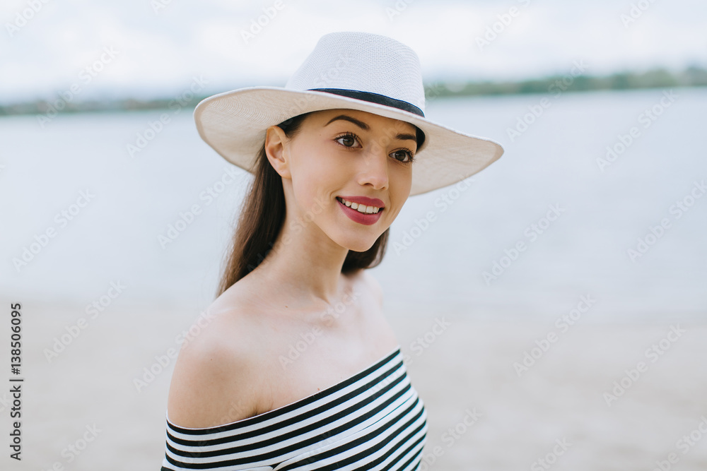 Stylish and fashionable girl in white hat posing on the summer beach.