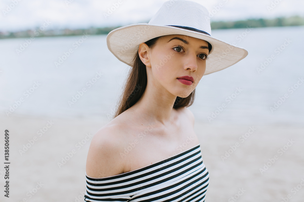 Stylish and fashionable girl in white hat posing on the summer beach.