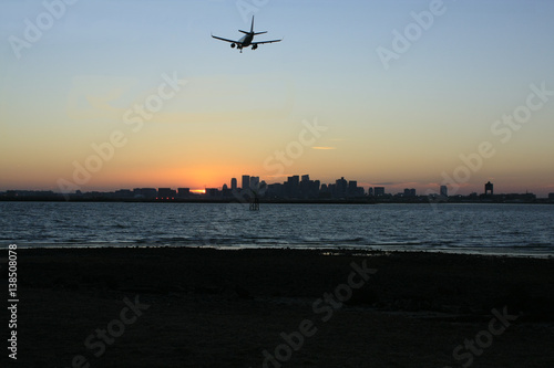 Night Flight: The airliner is approaching Boston's Logan International Airport across Boston Harbor as the sun sets behind the skyline of Boston.