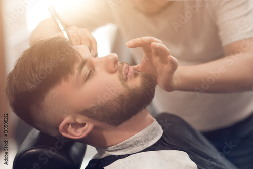 a master in the barbershop works with the client. shaves beard young guy. shaving with a straight razor