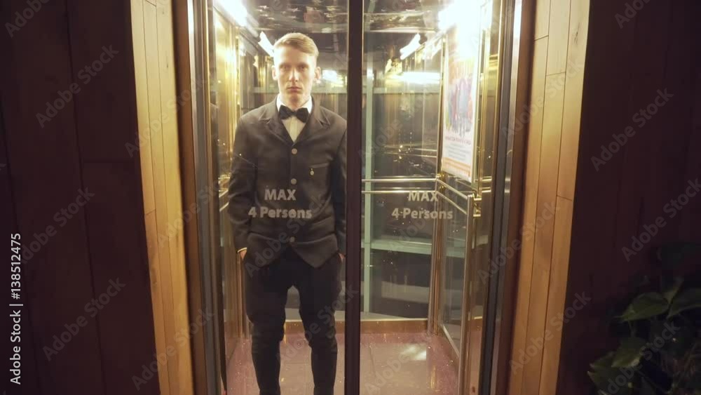 Young and successful businessman in a suit with a bow tie coming out of the Elevator with Glass Doors. Young and successful businessman in a suit with a bow tie coming out of the Elevator with Glass Doors.