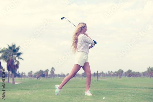 Fashion sport style beautiful woman standing holding golf club on outdoors green field background