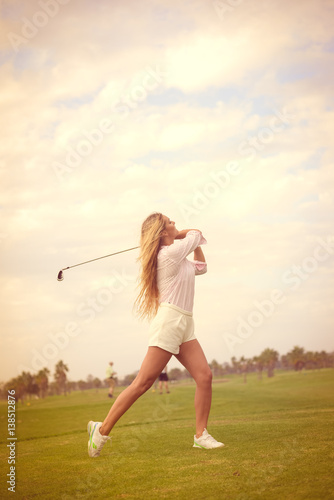 Fashion sport style beautiful woman standing holding golf club on outdoors green field background