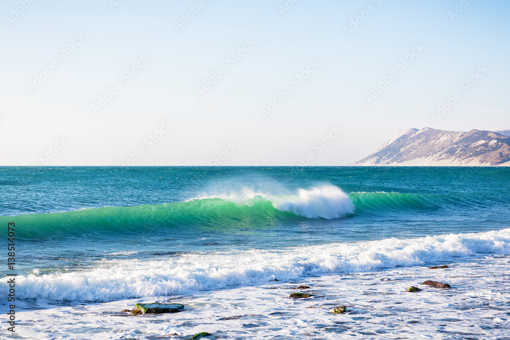 Powerful crystal wave breaks along the shore. Ocean and sky