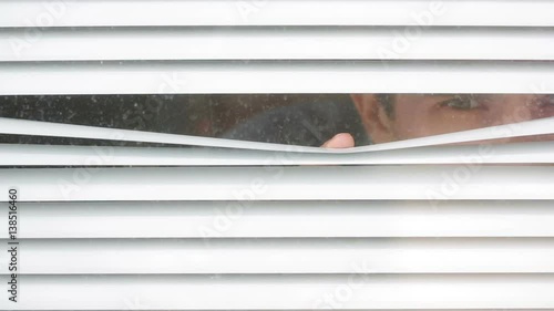 man looking out the window through the blinds to the street, spying. suspected photo