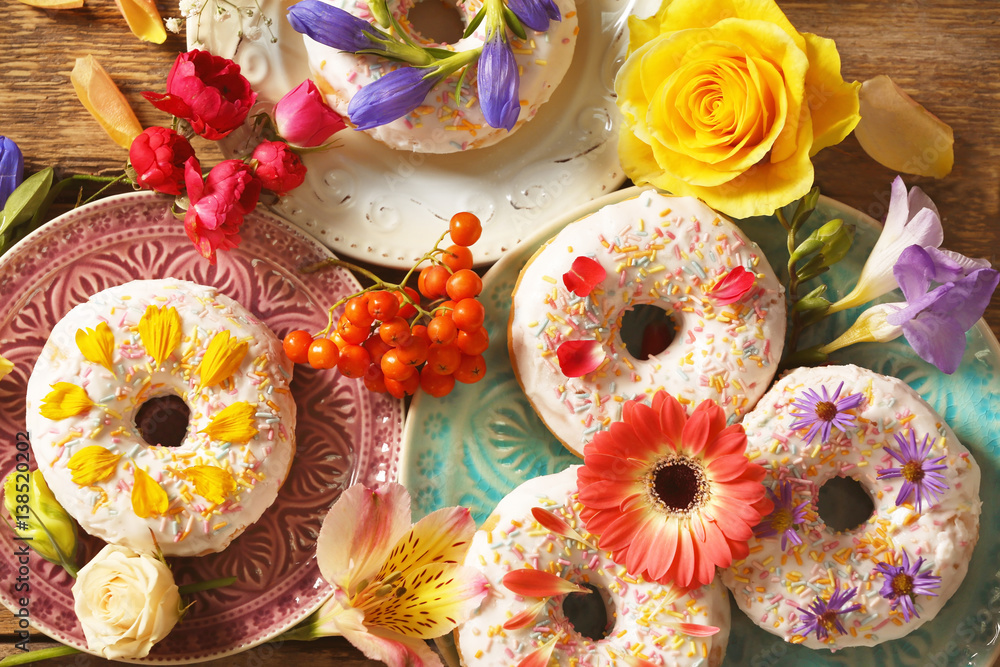 Composition of plates with delicious donuts and colourful flowers on wooden table Composition of plates with delicious donuts and colourful flowers on wooden table