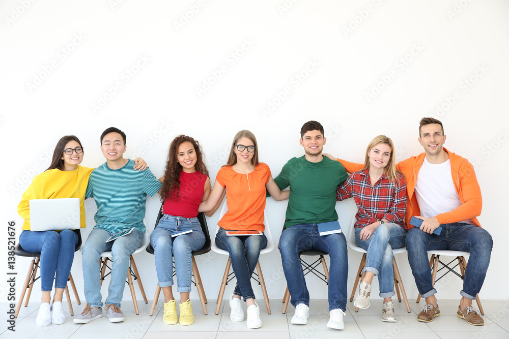 Obraz premium Group of people with books and gadgets sitting near light wall