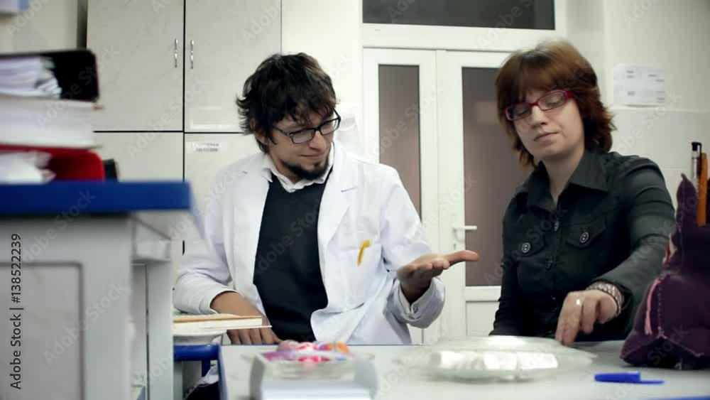 Scientific Laboratory / Research Team / Monitoring Room. Scientist woman gives man a coin lost on dispute in white lab. Scientific Laboratory / Research Team / Monitoring Room. Scientist woman gives man a coin lost on dispute in white lab.