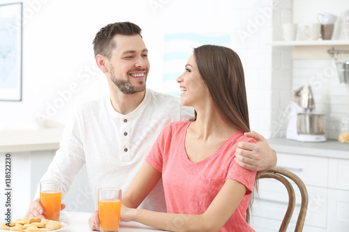 Beautiful young couple with orange juice sitting at kitchen table
