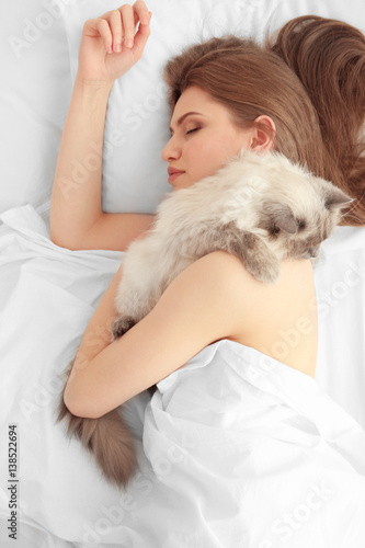 Beautiful young woman with cute cat lying in bed at home