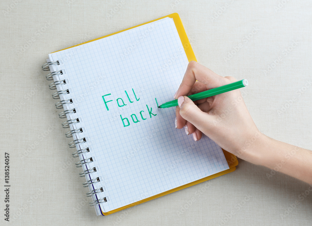 Female hand writing phrase FALL BACK in notebook Female hand writing phrase FALL BACK in notebook