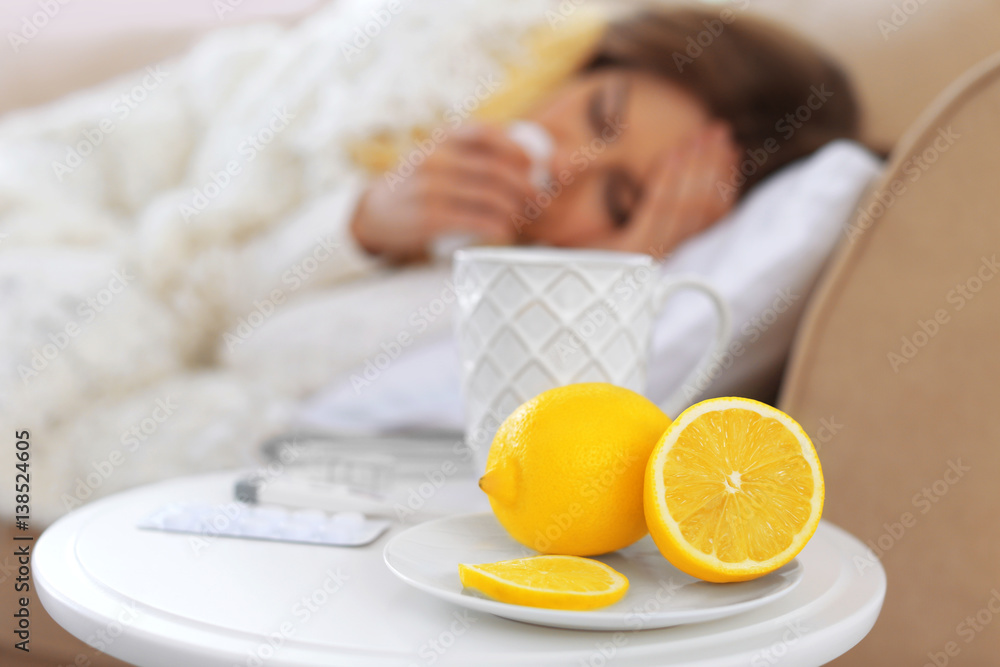 Lemons, cup of hot tea and medicines with blurred ill woman on background Lemons, cup of hot tea and medicines with blurred ill woman on background