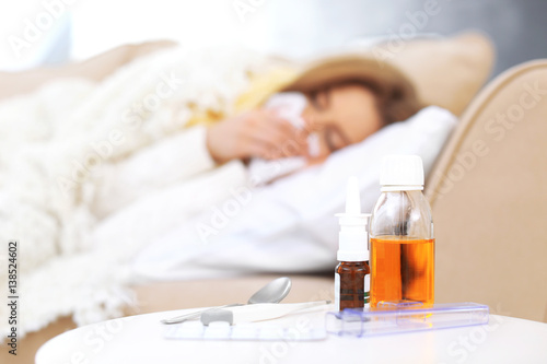 Set of medicines and electronic thermometer with blurred ill woman on background