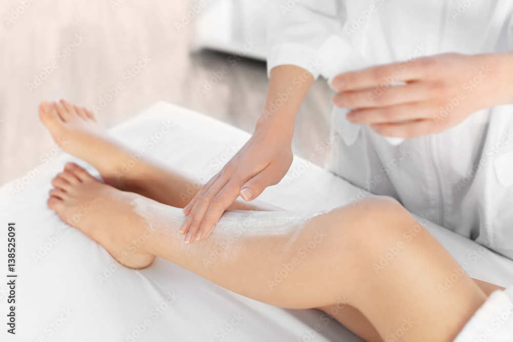 Beautician applying moisturizing cream on female legs in spa center Beautician applying moisturizing cream on female legs in spa center