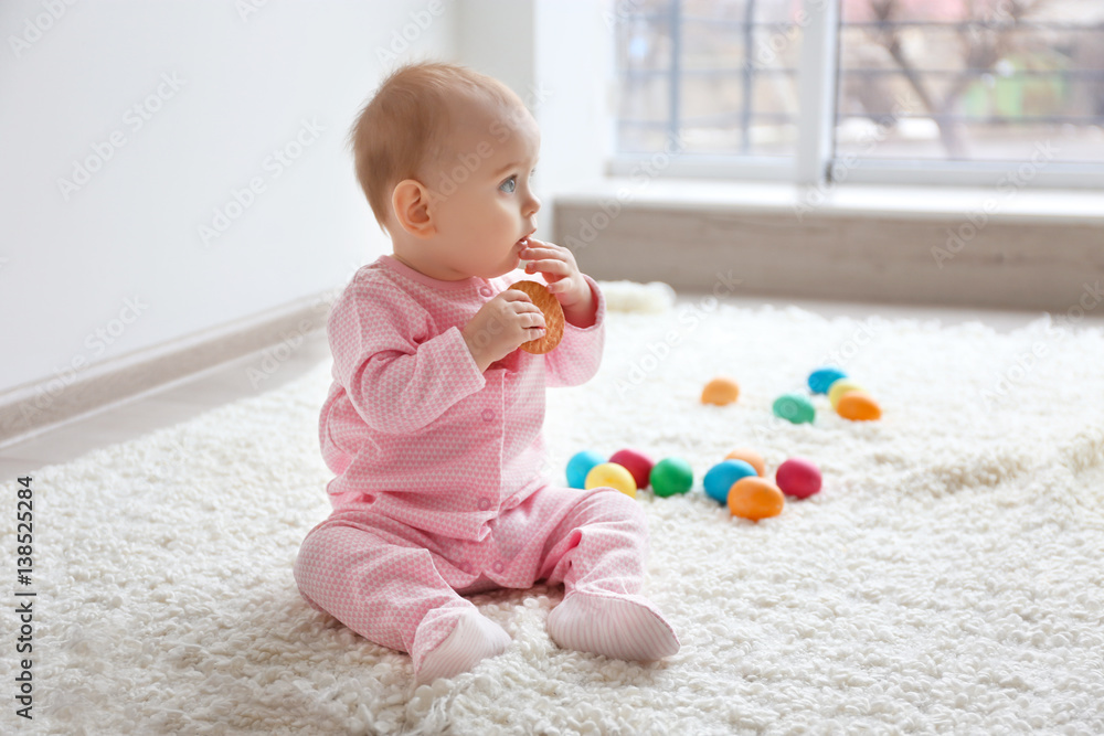 Fotografie Cute funny baby eating cookie while sitting on floor with Easter eggs