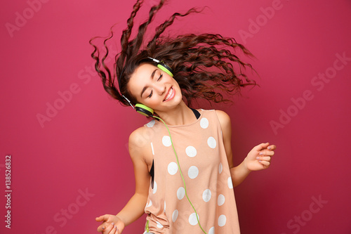 Beautiful young woman in headphones listening to music and dancing on color background