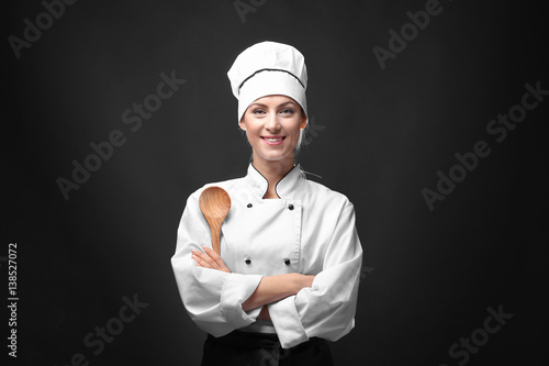 Portrait of female chef with wooden spoon on dark background