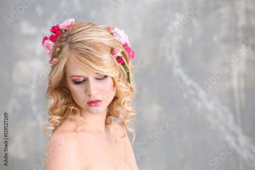 Beautiful young woman with flowers in hair on blurred background