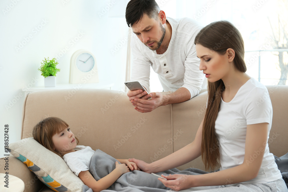 Mother measuring temperature of ill child while father calling a doctor Mother measuring temperature of ill child while father calling a doctor