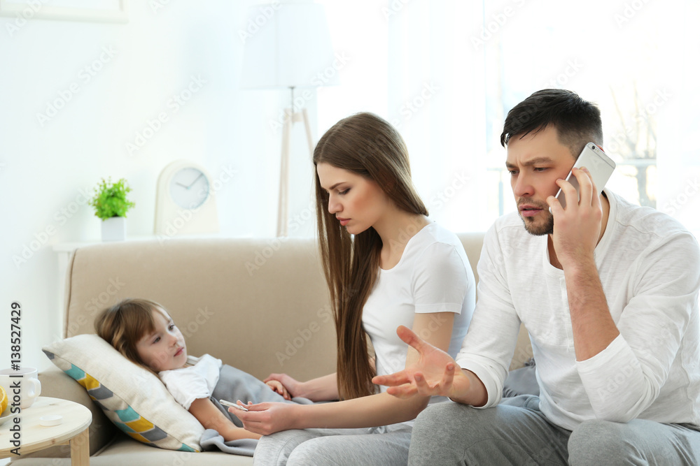 Mother measuring temperature of ill child while father calling a doctor