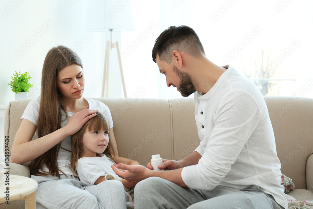 Parents giving medicines to ill girl while sitting on sofa at home Parents giving medicines to ill girl while sitting on sofa at home