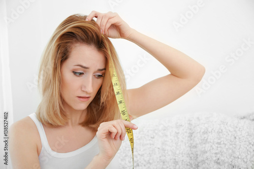 Beautiful young woman measuring length of hair at home photo