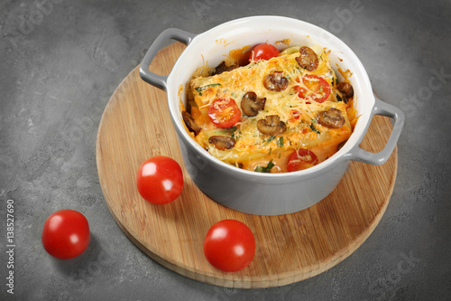 Delicious stuffed cannelloni with cherry tomatoes in ceramic pot on wooden board photo