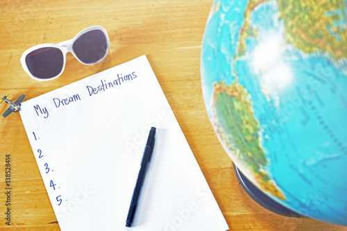 Dream destination list paper on wooden table beside world globe map, sunglasses and the plane toy