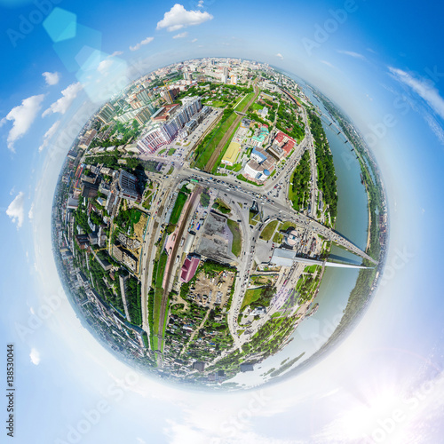 Aerial city view with crossroads and roads, houses, buildings, parks and parking lots, bridges. Copter shot. Little planet mode. Full sphere.