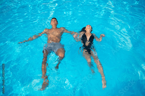 Couple in love refreshing in the swimming pool on the turquoise water at vacation. They are floating on the surface