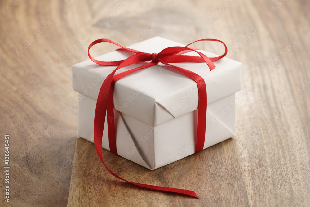 white paper gift box with thin red ribbon bow on old wood table, closeup  photo Stock Photo