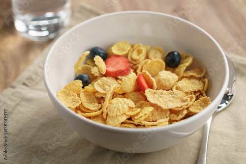 berries falling into corn flakes for breakfast in bowl on table, breakfast preparation