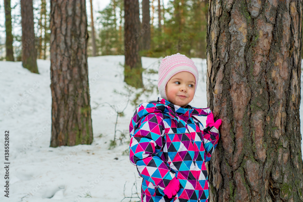 child standing near a tree in the winter forest child standing near a tree in the winter forest