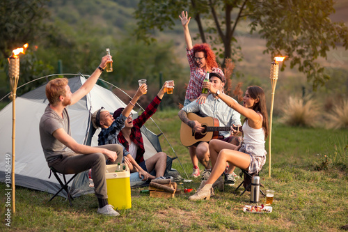 Young men and women toasting with beer on sunset in nature