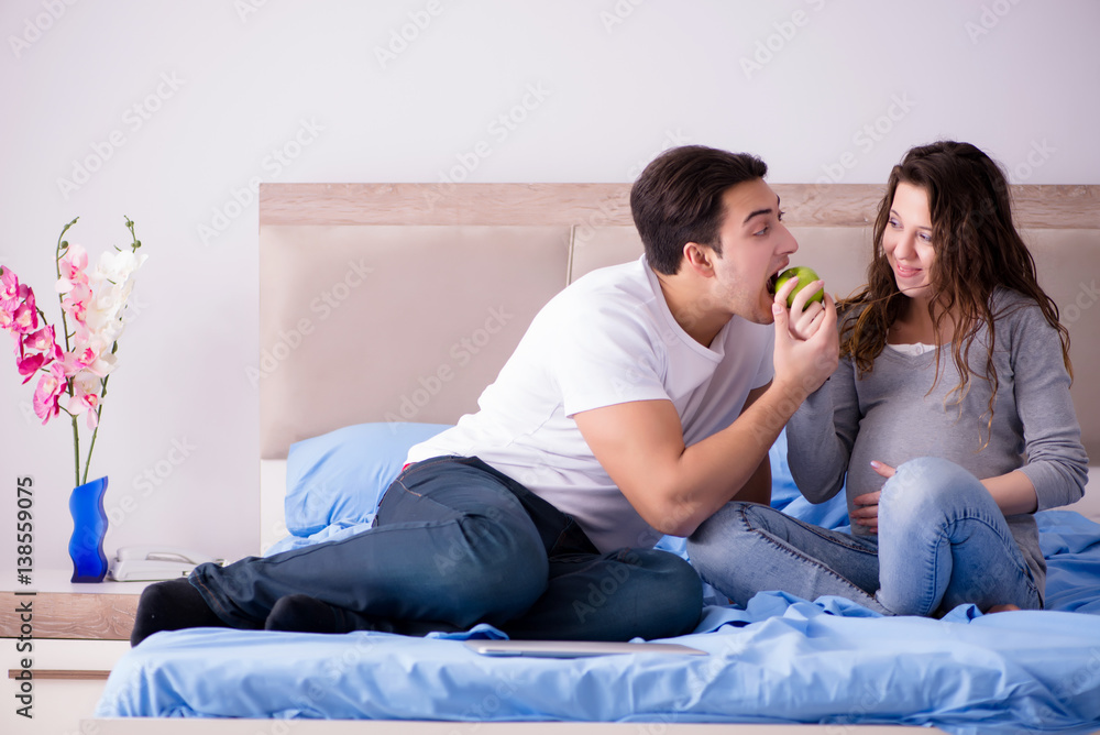 Young family with pregnant wife expecting baby in bed