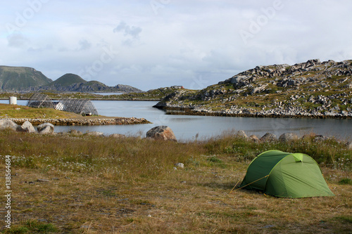 Zelt auf einer Wiese an einer Bucht mit Inselchen, im Hintergrund Gjesvaer und die Insel Storstappen in der Nähe des Nordkapp. Mageroya, Norwegen – Camping als Jedermannsrecht