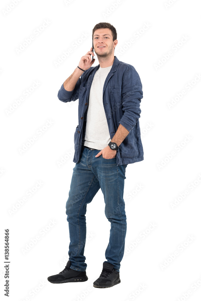 Happy smiling man in jeans and denim shirt talking on the phone looking at camera. Full body length portrait isolated over white background. Happy smiling man in jeans and denim shirt talking on the phone looking at camera. Full body length portrait isolated over white background.