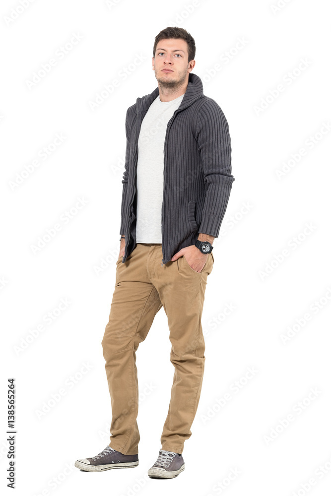 Handsome confident young man in ocher pants and gray sweater looking at camera. Full body length portrait isolated over white background. Handsome confident young man in ocher pants and gray sweater looking at camera. Full body length portrait isolated over white background.