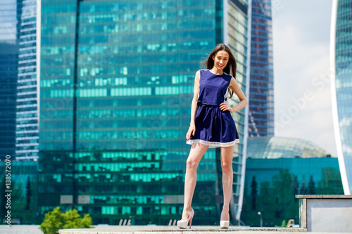 Young woman in a blue dress is stretching near skyscrapers © Andrey_Arkusha