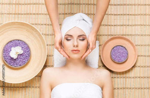 Beautiful, young and healthy woman on bamboo mat in spa salon having face massage. Spa, health and healing concept.