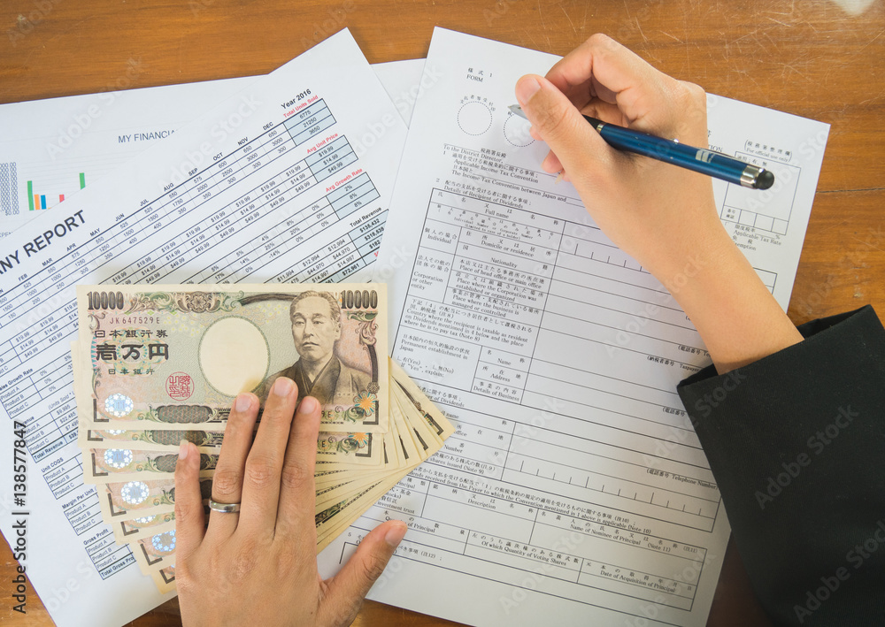 Obraz premium Woman hand hold pen fill in the details on the tax forms paper with yen moneyin business concept.
