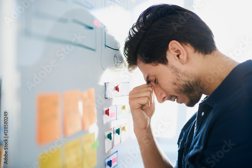 Frustrated, stressed designer struggle for new project ideas banging his head against whiteboard at office